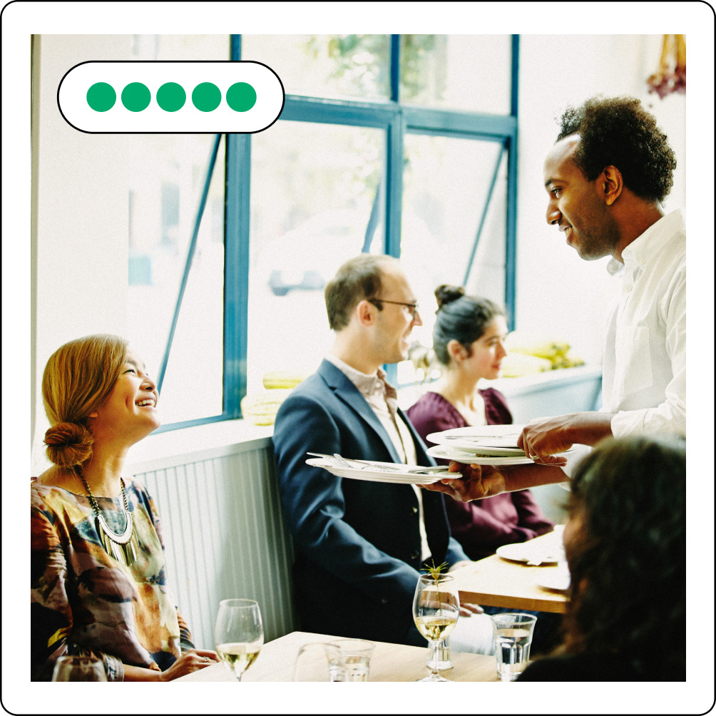 Image description: three people sitting in a restaurant smiling at a waiter holding plates. Five review bubbles are on the upper left side.