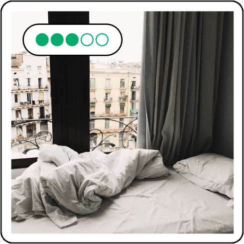 Image description: Hotel room with an unmade bed next to a large window that looks out into the city.