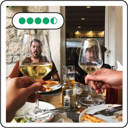 Image description: Two hands holding two glasses of wine in the foreground with two men in the background.